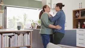 Two women embracing in kitchen leaning in and sharing love causing social media emojis rising right. Couple, affection, hug, home, natural, bright, cozy - Powered by Shutterstock - Get 15% off with code: PIKWIZARD15