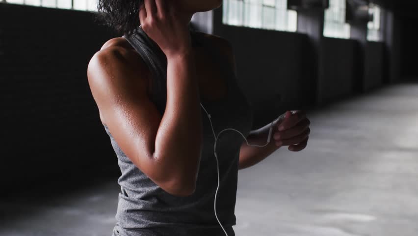 Woman holding earbud and tuning device, brain network animating across face torso for training. Warehouse, industrial, headset, fitness, neural, focus, daylight