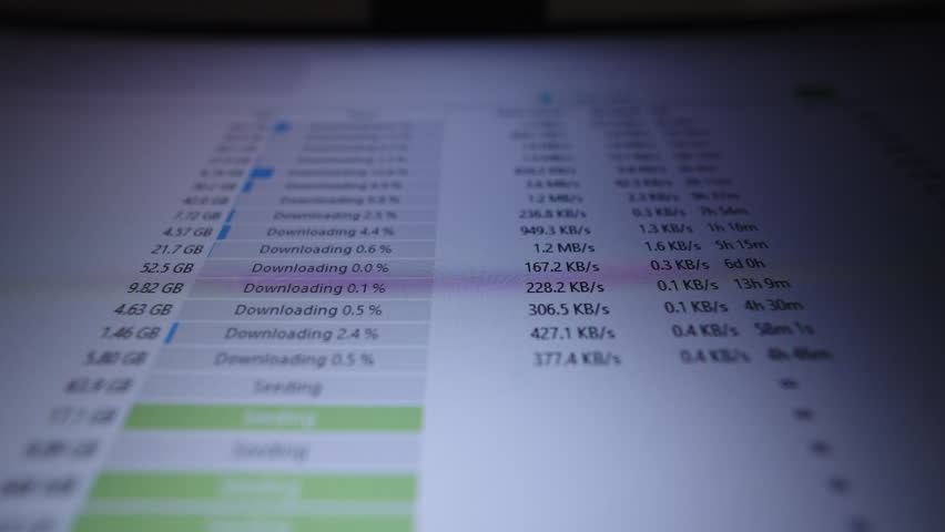 Computer screen displaying p2p client application actively downloading and uploading various files. Showing file sizes, download speeds, upload speeds, close-up, nobody. Shooting in slow motion.