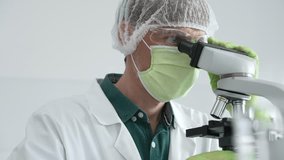 Laboratory scientist analyzing medical sample, wearing green protective gear and conducting research under microscope. Medicine, healthcare and science concept - Powered by Shutterstock - Get 15% off with code: PIKWIZARD15