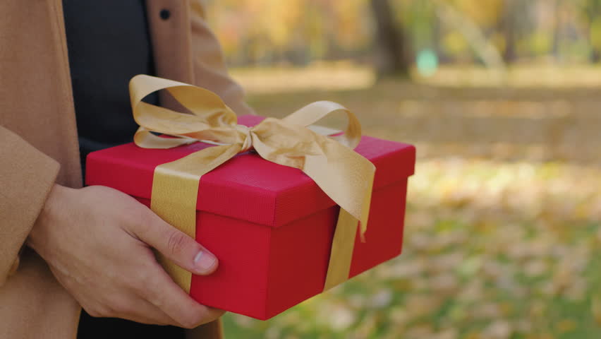 Close unrecognizable couple with gift box in city unknown man boyfriend congratulate woman girlfriend giving present with gold ribbon anniversary birthday surprise in autumn park love affectionate
