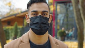 Close-up Hispanic man in facial medical mask looking at camera portrait Arabian guy in city autumn park Indian male posing pandemic covid19 ill sick medicine health protection prevention coronavirus - Powered by Shutterstock - Get 15% off with code: PIKWIZARD15