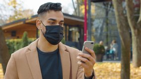 Hispanic man in face medical mask looking in mobile phone using app smartphone in park autumn fall season Arabian guy male chatting telephone social media chat outdoors positive online communication - Powered by Shutterstock - Get 15% off with code: PIKWIZARD15