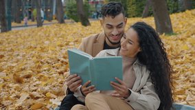Hispanic couple in autumn park picnic reading book together communicate sitting in yellow leaves on blanket outdoors romantic date Arabian man with Caucasian Indian woman read spending time together - Powered by Shutterstock - Get 15% off with code: PIKWIZARD15