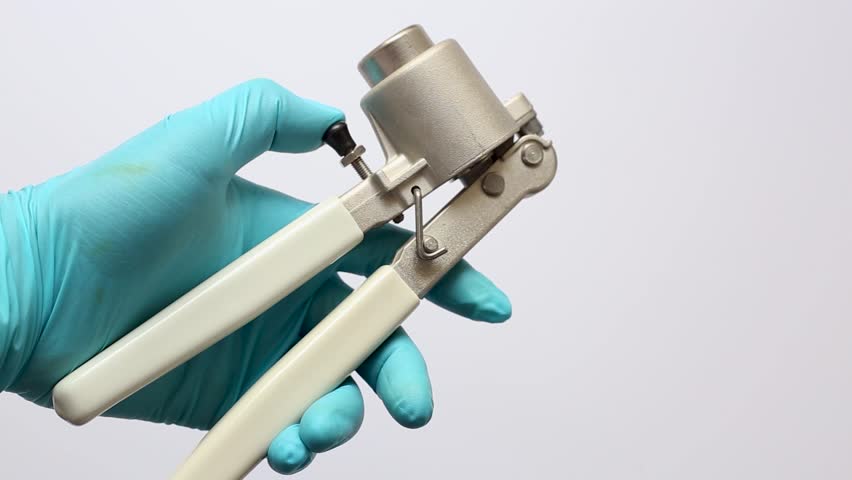 a scientist's hand holding a manual vial crimper, clearly showing the crimping head for sealing aluminum caps onto glass autosampler vials in a laboratory.