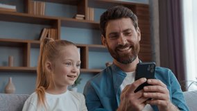 Caucasian happy family looking phone laughing father with daughter laugh watching mobile video funny content cute kid girl child look at smartphone with daddy positive having fun enjoying app gadget - Powered by Shutterstock - Get 15% off with code: PIKWIZARD15