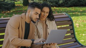 Happy emotional hispanic couple winning with laptop in city autumn park sitting on bench family arabian man caucasian woman multiracial married girl and guy with computer win victory bet achievement - Powered by Shutterstock - Get 15% off with code: PIKWIZARD15
