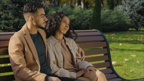 Cheerful hispanic couple in autumn park talking happy relaxing on bench in city communicate smiling Arabian man with lovely woman talk hugging love weekend fall season outdoors pointing away discuss - Powered by Shutterstock - Get 15% off with code: PIKWIZARD15
