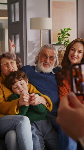 Unknown person holding mobile phone and pushing on sensor screen while taking pictures of big family. Caucasian people with kids posing for photo and doing funny faces with tongue out or wide smile.