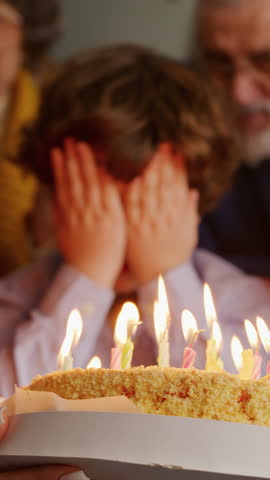 Little kid with curly hair covering face with palms and blowing all burning candles with help of older sister. Friendly family cheering up for birthday boy while looking at freshly baked cake.