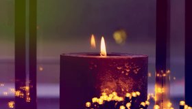 A detailed 4K view of a burning, dark-colored pillar candle, likely made from natural plant-based wax, creating a warm glow. - Powered by Shutterstock - Get 15% off with code: PIKWIZARD15