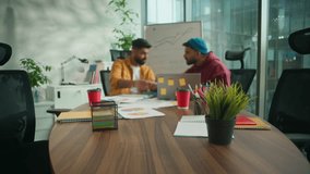 Informal casual multiracial business team in office meeting. African American woman coming in company sitting at table greeting high five gesture with Indian men colleagues talking pointing laptop - Powered by Shutterstock - Get 15% off with code: PIKWIZARD15