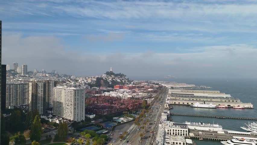 A straight-down aerial view of the iconic San Francisco Ferry Building clocktower located along the Embarcadero. The drone shot captures the roof, clock face, surrounding plaza, and waterfront area wi