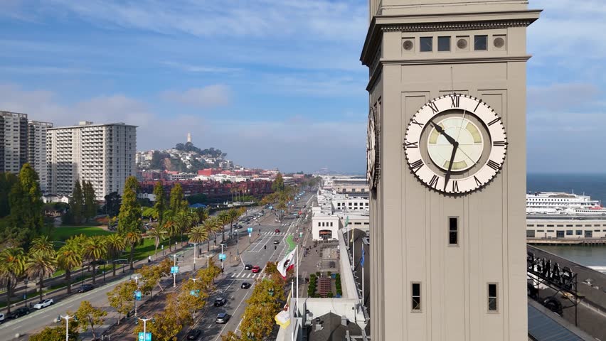 A cinematic aerial orbit around the historic San Francisco Ferry Building clocktower along the Embarcadero. The drone circles the tower, revealing detailed architecture, the clock face