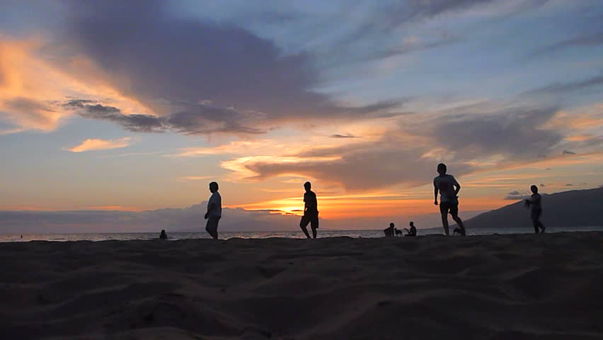 Unrecognizable people on sandy beach during sunset in Hawaii.