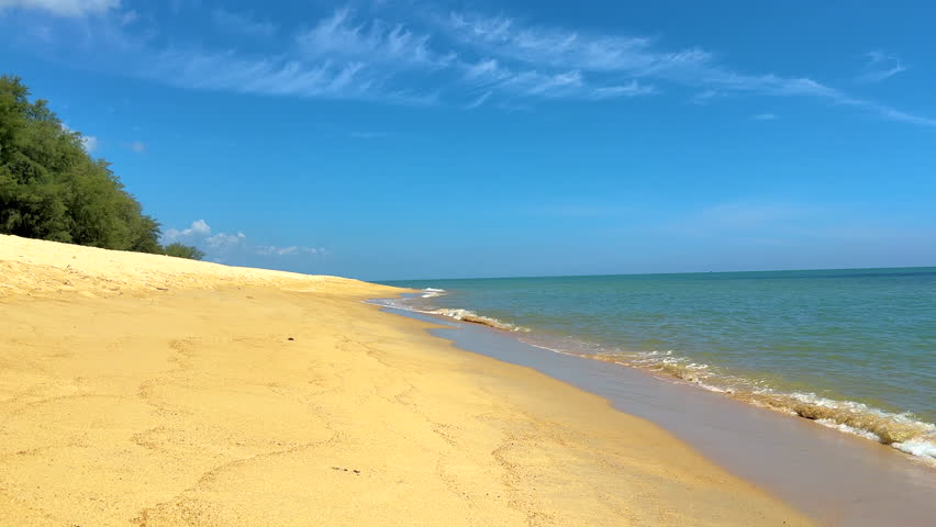 Gentle waves washing onto a sandy beach with a distant island under a clear blue sky.