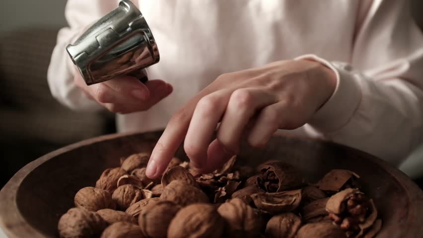 Closeup video of cracking walnuts using special tool. Nuts in a vintage wooden bowl. Healthy snack rich in fiber, fat and nutrients. Removing shell from walnuts. 