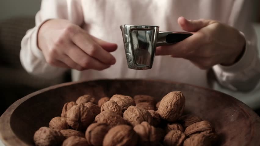 Closeup video of cracking walnuts using special tool. Nuts in a vintage wooden bowl. Healthy snack rich in fiber, fat and nutrients. Removing shell from walnuts. 