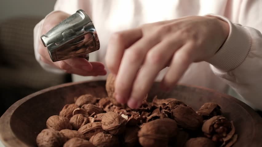 Closeup video of cracking walnuts using special tool. Nuts in a vintage wooden bowl. Healthy snack rich in fiber, fat and nutrients. Removing shell from walnuts. 