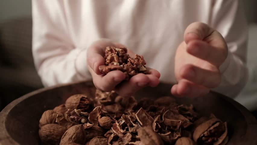 Closeup video of cracking walnuts using special tool. Nuts in a vintage wooden bowl. Healthy snack rich in fiber, fat and nutrients. Removing shell from walnuts. 