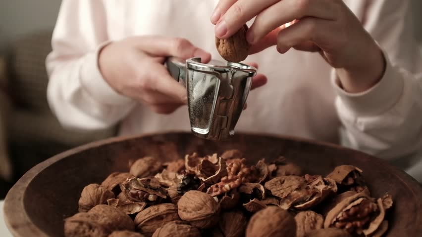 Closeup video of cracking walnuts using special tool. Nuts in a vintage wooden bowl. Healthy snack rich in fiber, fat and nutrients. Removing shell from walnuts. 