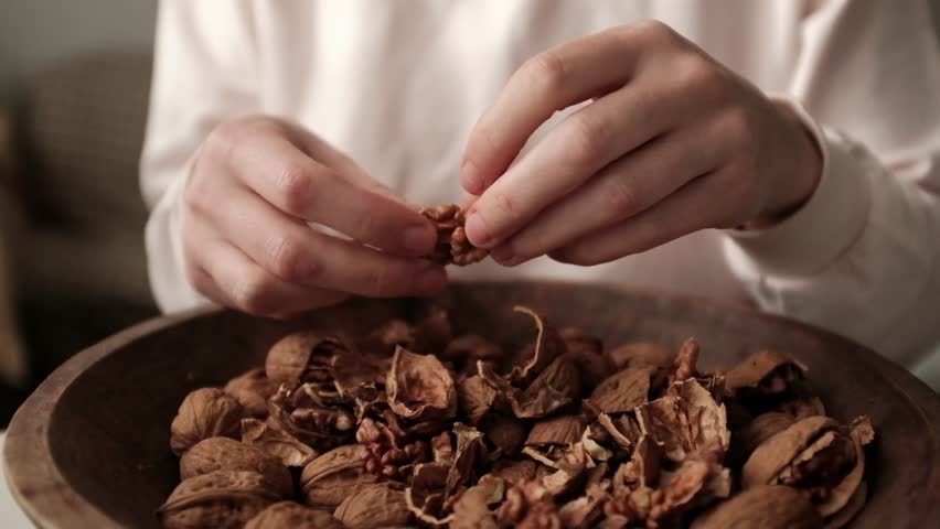 Closeup video of cracking walnuts using special tool. Nuts in a vintage wooden bowl. Healthy snack rich in fiber, fat and nutrients. Removing shell from walnuts. 