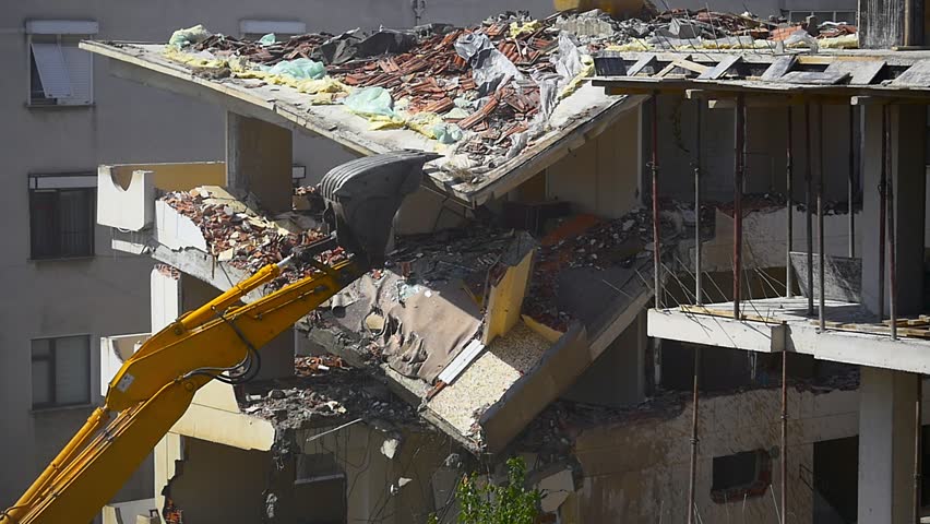 Demolition. Destruction of concrete floors of a ruin house. Builders demolishes a city house using a hydraulic excavator and dust fills the air. Crane arm dismantling a building. Slow Motion