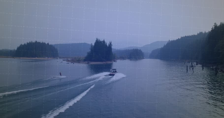 Driver towing rider through inlet carving wakes while animated bars covering rider with sports data. Powerboat, towrope, spray, aerial, coastal, islands, forests