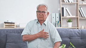 Asian Elderly man holding chest pain couch showing concern about health care and heart symptom while seated home senior male clutching chest sofa experiencing discomfort living room showing concern - Powered by Shutterstock - Get 15% off with code: PIKWIZARD15