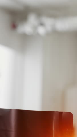 Worker filling roasted coffee beans into retail package using metal scoop inside coffee production shop during packaging process.