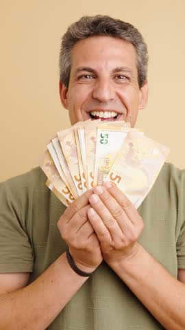 Middle-aged man with graying hair smelling and fanning his face with a stack of fifty euro banknotes, expressing greed and happiness. Vertical