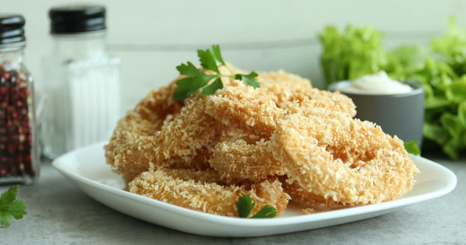 Woman dipping tasty deep fried squid ring into sauce at grey textured table, selective focus
