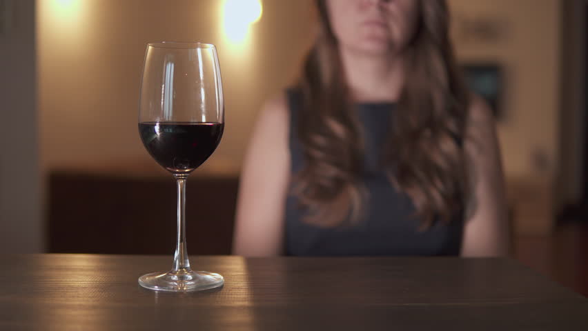 Unknown woman is refusing wine. Glass of red wine on wooden table at home. Personal choice for sober lifestyle. Health consciousness. Modern social trend away from alcohol.