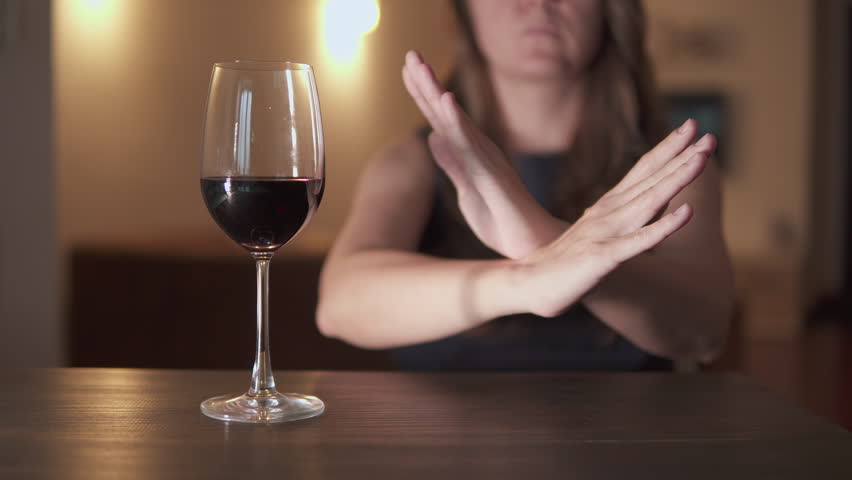 Unknown woman is refusing wine. Glass of red wine on wooden table at home. Personal choice for sober lifestyle. Health consciousness. Modern social trend away from alcohol.