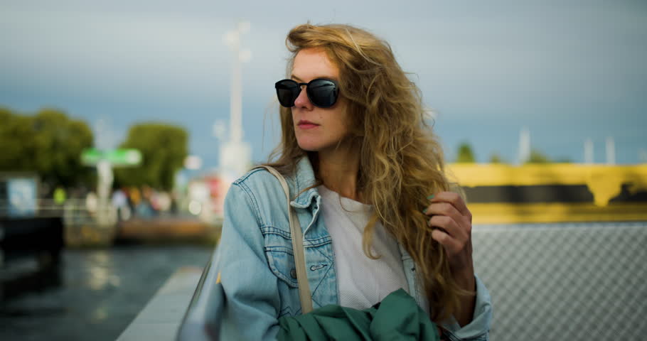 A cheerful young woman with curly hair smiles while enjoying a scenic ferry journey through Amsterdam