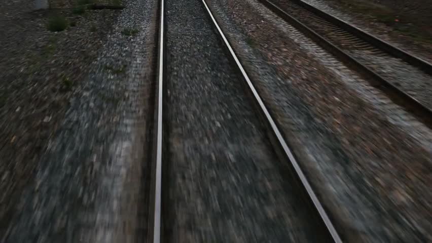 Train passing through the countryside on moving railroad tracks during daytime, showcasing transportation, travel, and scenic rural landscapes in motion.