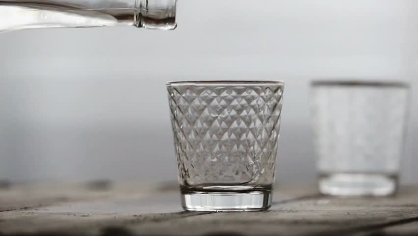 Alcohol being poured into a glass with ice, highlighting clear vodka flow, cold beverage texture, and elegant drink preparation in a close-up shot.