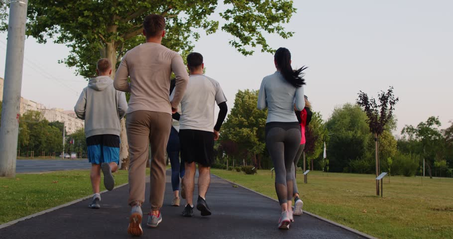 Group of active young people running outdoors on path in park in morning, leading healthy lifestyle, breathing fresh air, enjoying sport, dressed in activewear. Healthy body habits