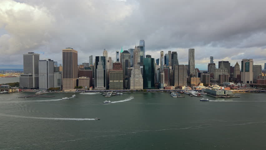 Aerial view of financial Manhattan, New York City, New York showing downtown skyline, open river surface and bright soft daylight stretching across the wide waterfront scene.