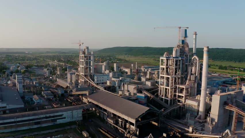 Aerial drone view of a large cement plant with tall industrial structures, capturing production facilities, machinery layout, and a strong industrial atmosphere.