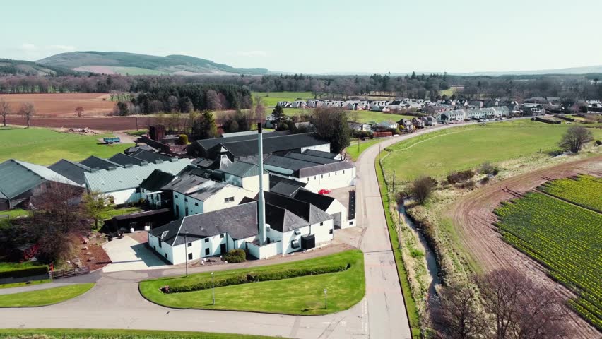 Aerial view flying away from Fetter cairn Whisky Distillery on a sunny spring day, showcasing distillery buildings, Fetter cairn town, and scenic Aberdeen shire, Scotland.