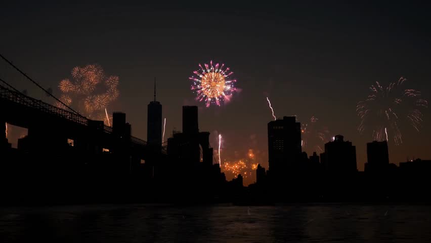 Fireworks explode over the city skyline at sunset, celebrating a holiday with vibrant colors, festive atmosphere, and spectacular pyrotechnic display.
