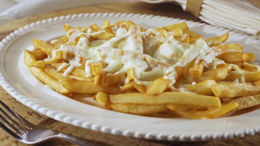 Crispy fries served on a plate with sour sauce being poured on top, capturing rich texture, creamy drizzle, and delicious comfort-food aesthetics for food and culinary visuals.