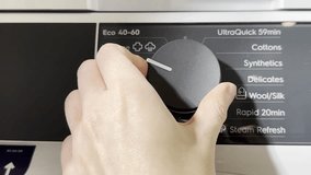 A hand turns the control knob on a washing machine, selecting a wash program from the panel options as part of the laundry preparation process. - Powered by Shutterstock - Get 15% off with code: PIKWIZARD15