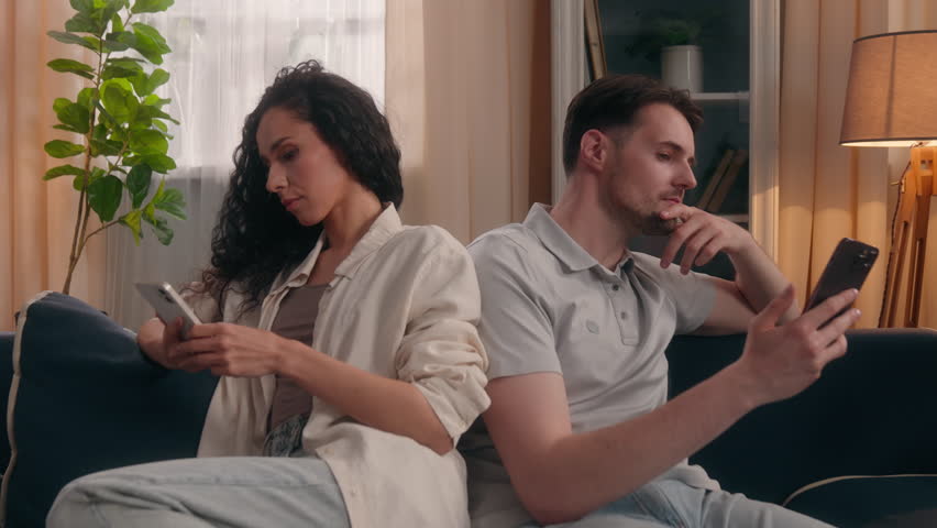 Gadget addicted family Caucasian male and Hispanic female couple ignoring each other at home use mobile phones social media dependence internet addiction separated scrolling devices distracted indoor