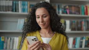 Happy Latina Hispanic woman student using mobile phone smartphone typing sms chatting in library university high school college online networking smile female girl laugh technology browsing elearning - Powered by Shutterstock - Get 15% off with code: PIKWIZARD15