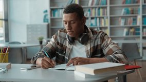 African American man talking on smartphone writing notes in university library focused student male guy speaking mobile phone call exam preparation study learning education books technology headphones - Powered by Shutterstock - Get 15% off with code: PIKWIZARD15