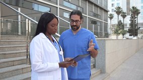 Video of Two diverse healthcare workers reviewing patient data on a tablet outside hospital - Powered by Shutterstock - Get 15% off with code: PIKWIZARD15