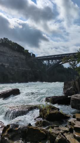 Dramatic Niagara Gorge Cliffs and Rushing White Water Rapids at White Water Walk Ontario Canada - Vertical Pan of Steep Rock Formations Lush Green Foliage and Foamy River Currents in Misty Environment