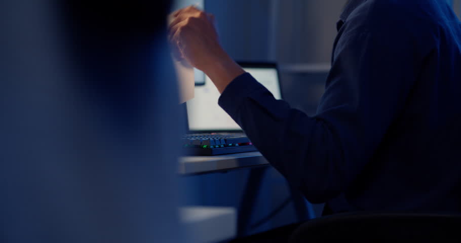 A close-up shot of an Asian business person's hand pointing at data and charts displayed on a computer screen while working late. Conveys analysis and finance.